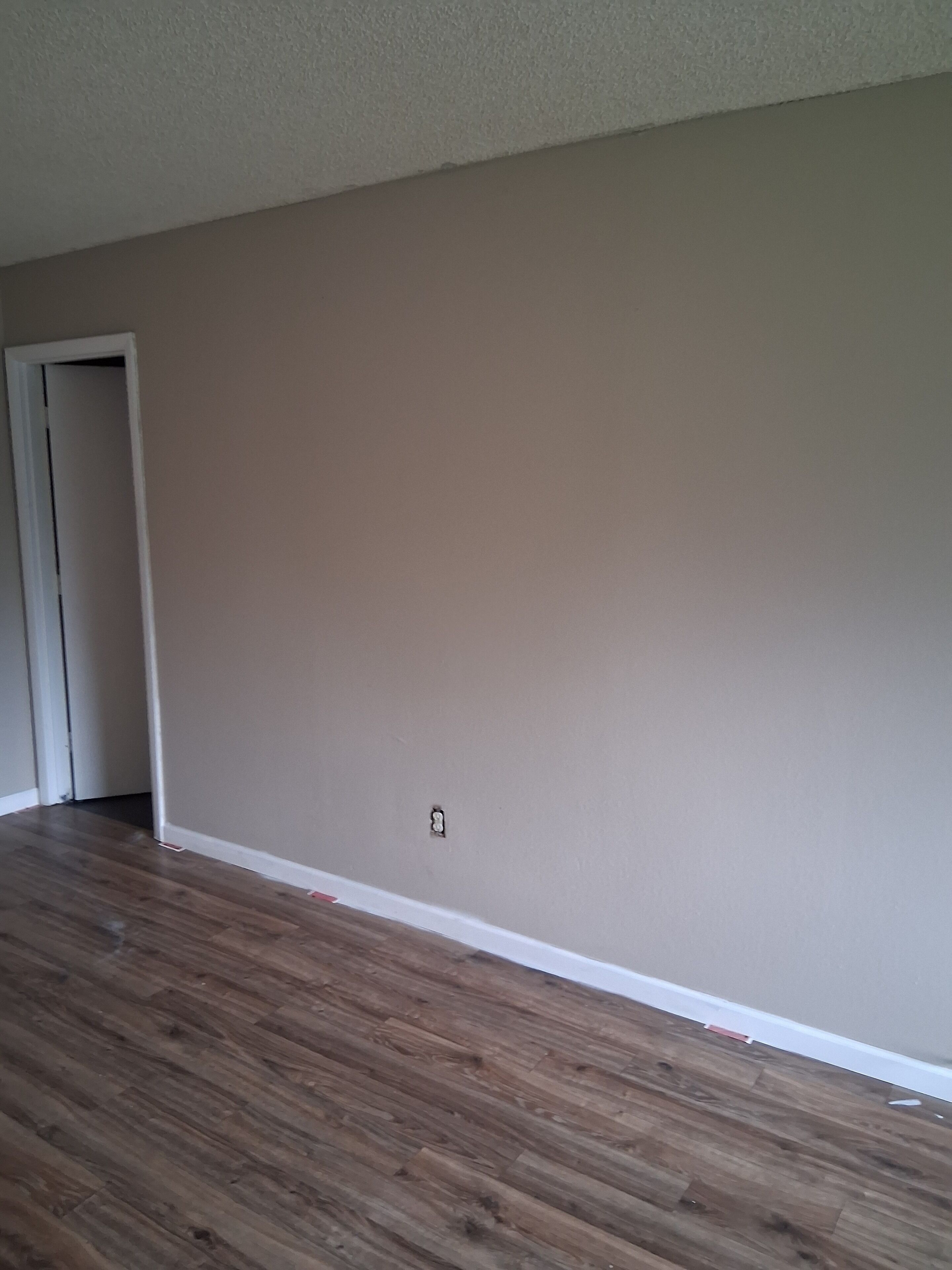 A room with wooden flooring, a beige wall, and a door.