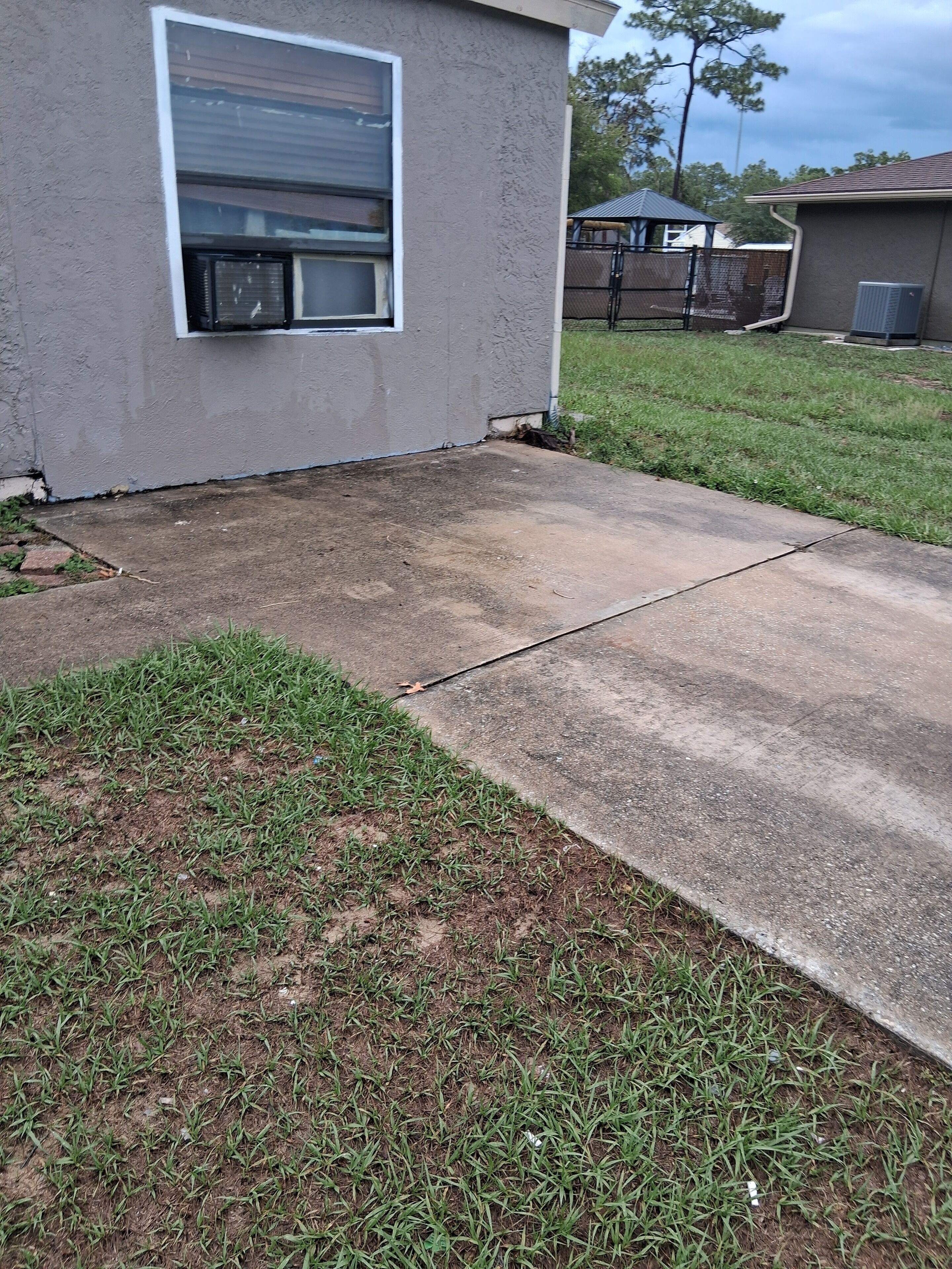 Une allée menant à une maison et aboutissant à un garage, avec une pelouse verdoyante au premier plan et une clôture en arrière-plan.