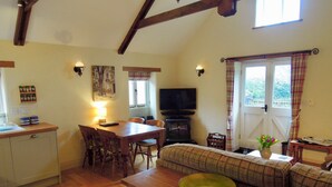 A cozy living room with a wooden dining table, a sofa, and a television. - The Cider Barn in Saint Austell (St Austell)