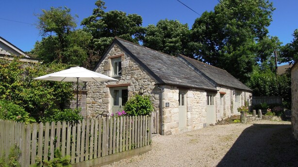 A stone cottage with a gravel driveway, a wooden fence, and a white umbrella. - The Cider Barn in Saint Austell (St Austell)