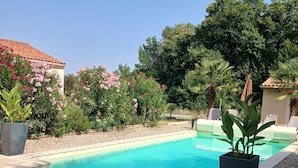 Ein Schwimmbecken mit gefliestem Deck, umgeben von üppiger Vegetation und blühenden Pflanzen.
