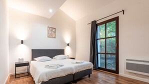 A bedroom with a large bed, two bedside tables, a wall-mounted light, a window with curtains, and a radiator. - Margaux Deluxe 8p - Four Bedroom Villa, Sleeps 8 (Salles)