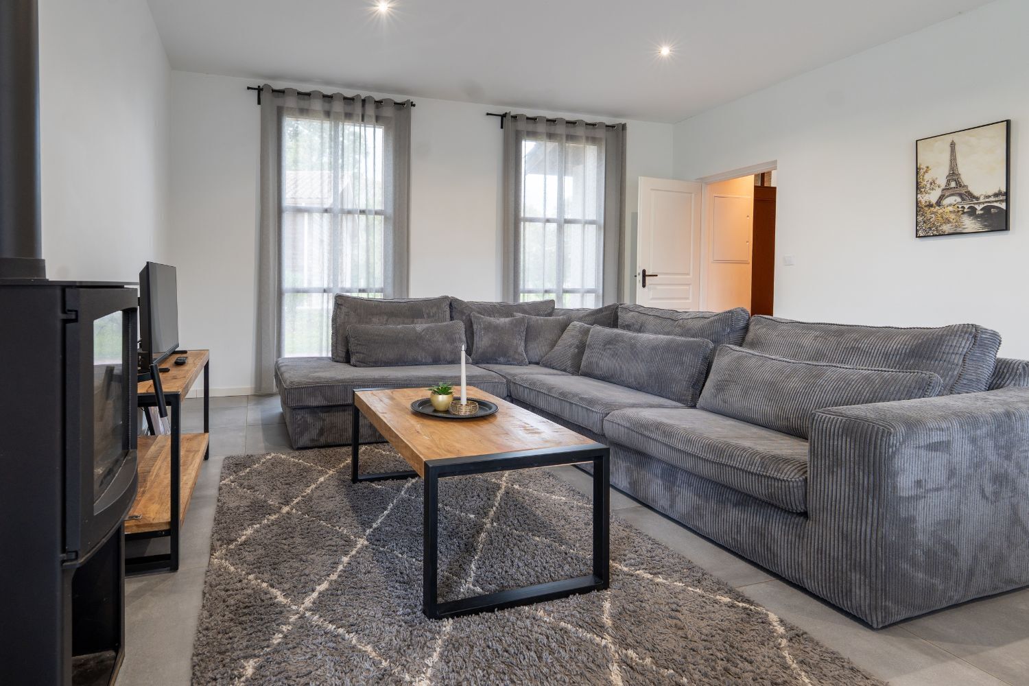 Een moderne woonkamer met een grijze modulaire bank, een houten salontafel en een flatscreen televisie.