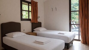 Een hotelkamer met twee bedden, een raam met gordijnen, een houten nachtkastje en uitzicht op de omgeving.