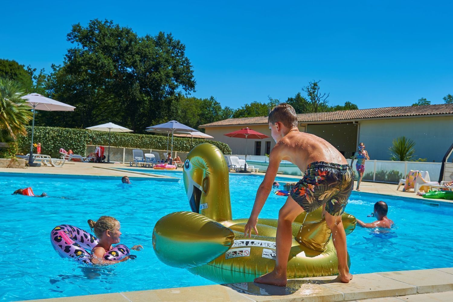 Une piscine avec des jeux gonflables, des chaises longues et des parasols.