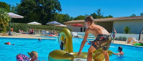 Une piscine avec des jeux gonflables, des chaises longues et des parasols.