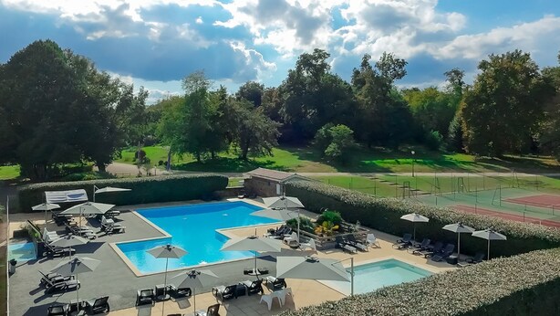 Un espace piscine doté de nombreuses chaises longues et de parasols, entouré de haies et d’arbres bien entretenus.