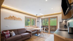 A modern kitchen with a built-in oven, a dining area with a table and chairs, a sofa with cushions, and large windows offering a view of the outdoors. - Apartment 'Weissbrunn Alexander' with Mountain View, Shared Terrace and Wi-Fi (St. Maddalena)