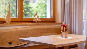A wooden bench with a small table beside it, a window with a view of greenery, and a decorative tree outside the window. - Apartment 'Weissbrunn Alexander' with Mountain View, Shared Terrace and Wi-Fi (St. Maddalena)