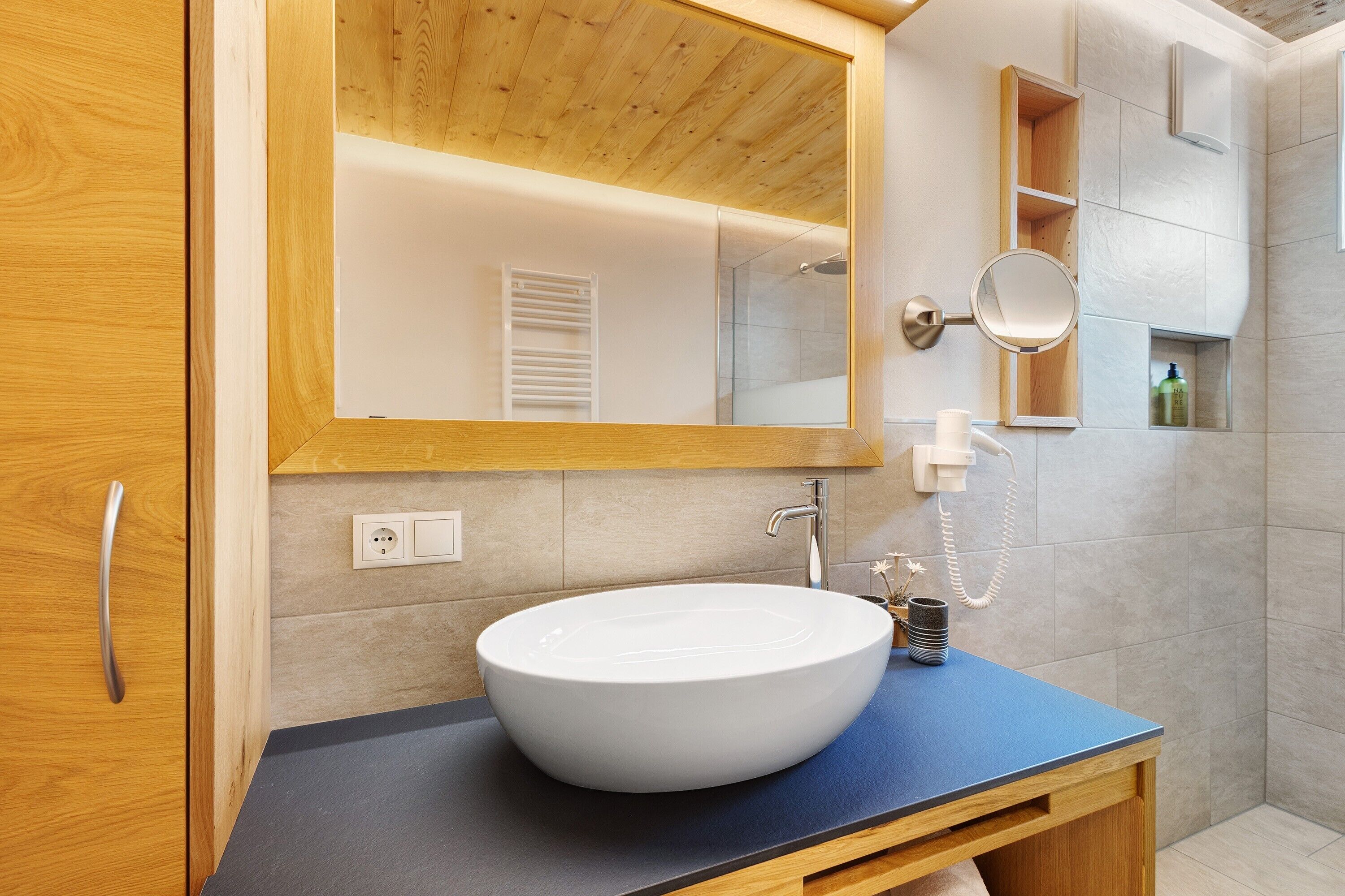 Een badkamer met een houten wastafel, een witte wasbak, een spiegel en een douchehoek.