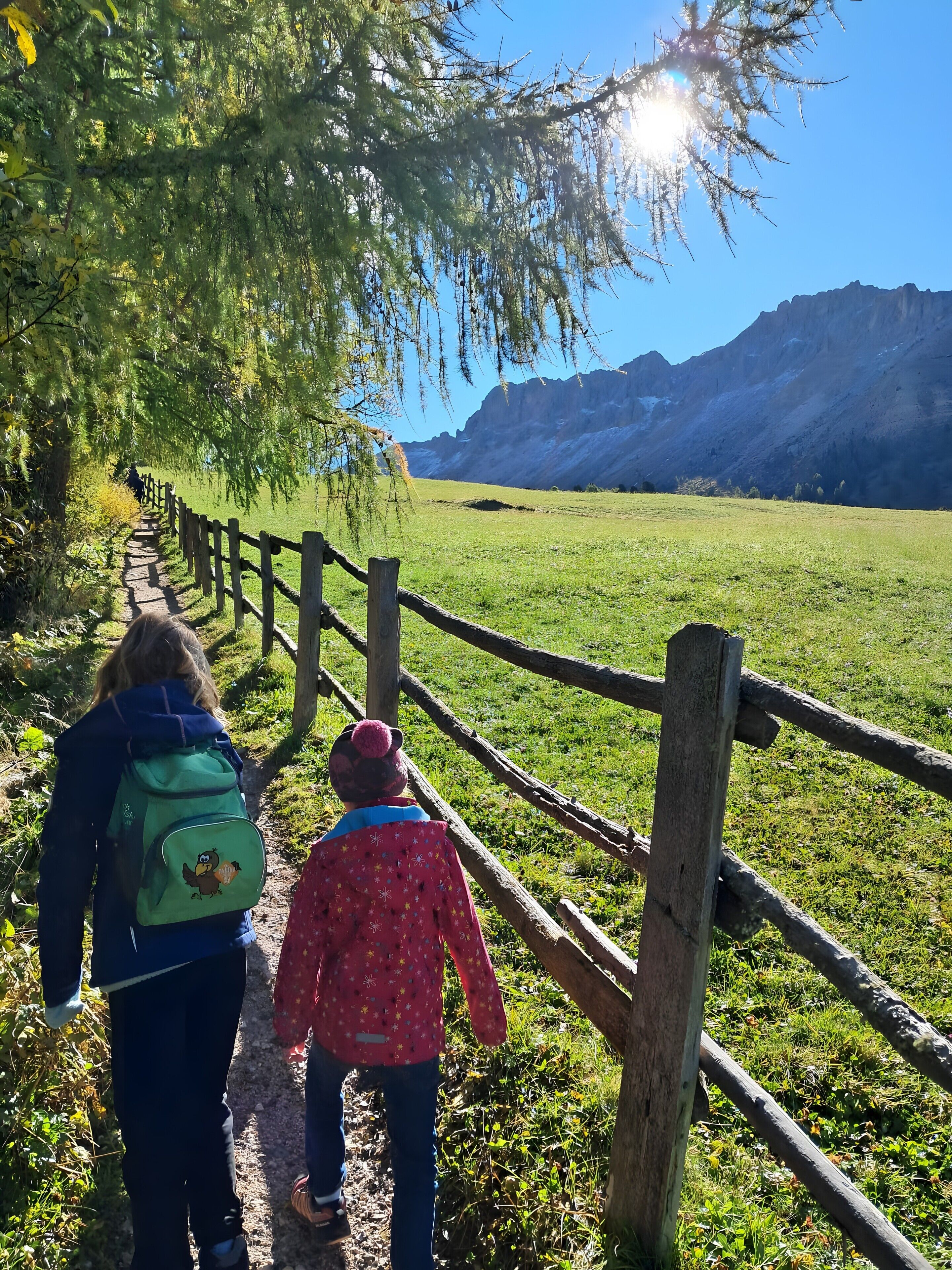 A pathway with a wooden fence, a person with a backpack, and a child.