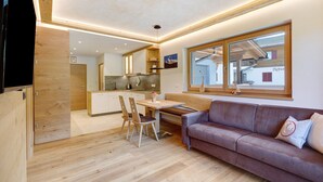 A modern interior with a wooden floor, a sofa, a dining table with chairs, and a kitchen area. - Apartment 'Weissbrunn Lisa' with Mountain View, Shared Terrace and Wi-Fi (St. Maddalena)