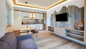 A modern kitchen with white cabinets, a wooden dining table, and a built-in TV. - Apartment 'Weissbrunn Dominik' with Mountain View, Shared Terrace and Wi-Fi (St. Maddalena)