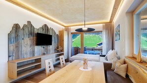 A modern living room with a wooden dining table, a sofa, and a TV mounted on a wooden wall. - Apartment 'Weissbrunn Dominik' with Mountain View, Shared Terrace and Wi-Fi (St. Maddalena)