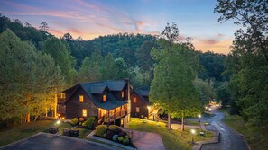 A lodge with multiple rooms, a driveway, and a forested backdrop.