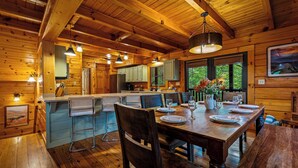 Interior de una cabaña de madera con comedor, cocina y barra.
