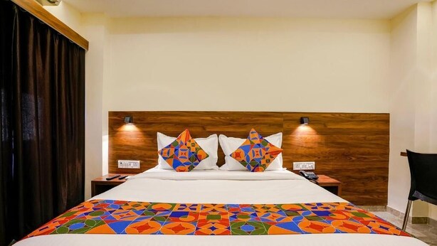 A hotel room with a wooden headboard, two bedside lamps, a bed with a colorful geometric-patterned bedspread, and a dark curtain on the left. - Antlers Hotel (Mumbai)