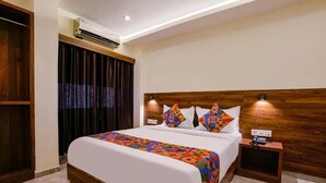 A neatly made bed with a colorful geometric-patterned bedspread, a wooden headboard, and two bedside lamps. - Antlers Hotel (Mumbai)