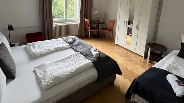 Habitación de hotel con dos camas, un escritorio, una silla y un armario.