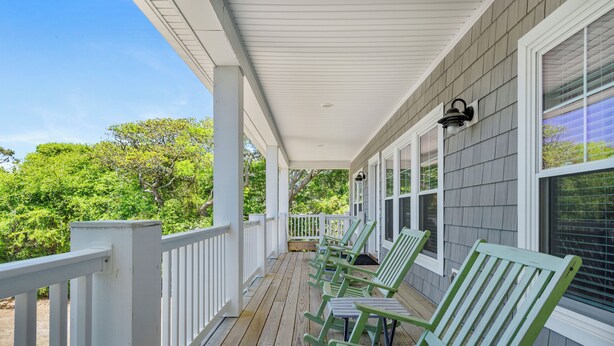 A covered porch with white railings and green chairs, overlooking a lush green landscape. - 4 BR Cottage w/ Pool, Hot Tub, Tiki Bar, 2 King Suites - Walk to Beach (Emerald Isle)