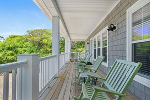 Eine überdachte Veranda mit weißen Geländern und grünen Stühlen, mit Blick auf eine üppige grüne Landschaft.