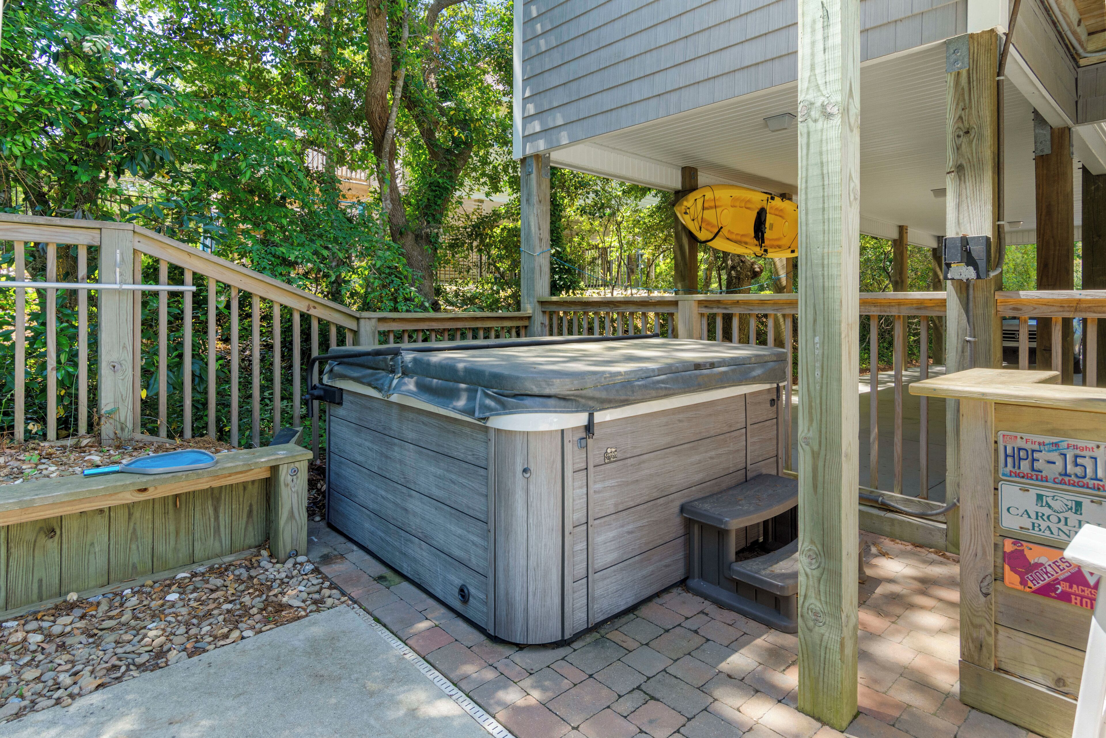 Ein Whirlpool mit Holzterrasse und überdachtem Bereich, umgeben von Holzzaun und Bäumen.