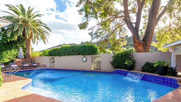 Une piscine avec un bord carrelé, une horloge au mur et un palmier.