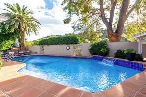 Une piscine avec un bord carrelé, une horloge au mur et un palmier.