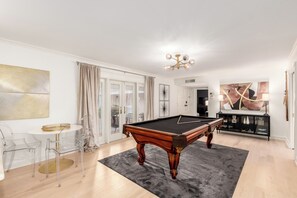 Una sala de estar moderna con mesa de billar, sillas traslúcidas, una mesa de comedor y un cuadro abstracto de gran tamaño.