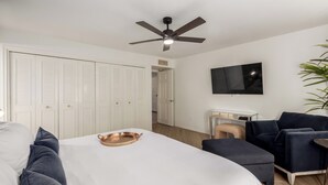 Une chambre à coucher avec un lit, un ventilateur de plafond, une télévision, un bureau et une chaise.