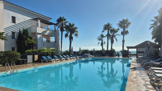 A swimming pool with lounge chairs and umbrellas, surrounded by palm trees and a building with balconies. - Magnificent T3 air-conditioned ground floor apartment with swimming pool and private beach ideal location (San-Nicolao)