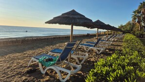 A beach with rows of sun loungers and thatched umbrellas, a sandy shore, and a calm sea. - Magnificent T3 air-conditioned ground floor apartment with swimming pool and private beach ideal location (San-Nicolao)