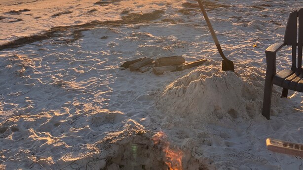 A beach scene with a sunset, a fire pit, and a chair.