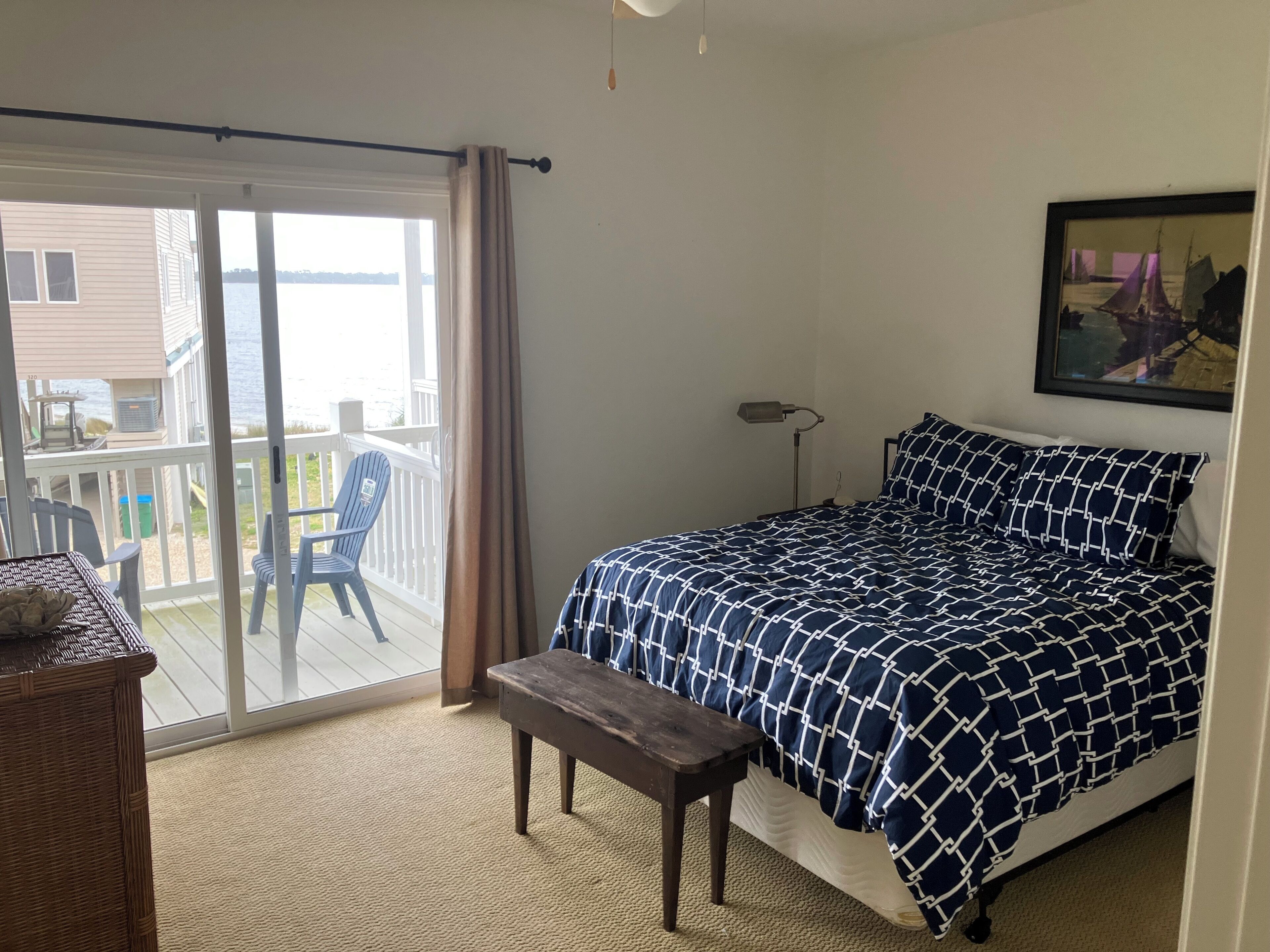 A bedroom with a bed, a bench, a chair, a lamp, and a view of the outside.