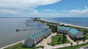 A coastal hotel with multiple buildings, a pier extending into the water, and a beach in the background.