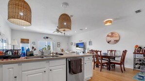 A modern kitchen with white cabinets, a wooden dining table, and wicker ceiling lights.