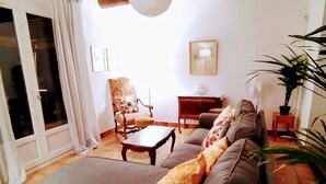 A living room with a sofa, a wooden coffee table, and a chair. There is a plant on the right and a door on the left.