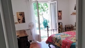 A bedroom with a bed, a wooden dresser, a fan, and a window with curtains.