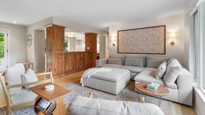Un amplio salón con un sofá grande de color gris, un mueble de madera y un tapiz decorativo en la pared.