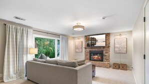 Una sala de estar con un sofá color beige, una chimenea y un ventanal con cortinas.