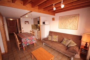 A cozy living room with a brown sofa, a wooden coffee table, and a dining area with a patterned tablecloth.