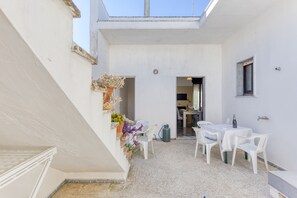 Un bâtiment blanc doté d’un patio couvert, d’un escalier et d’une table entourée de chaises.