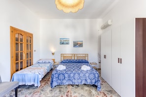 Une chambre avec deux lits, une armoire en bois, un climatiseur fixé au mur et un luminaire au plafond.