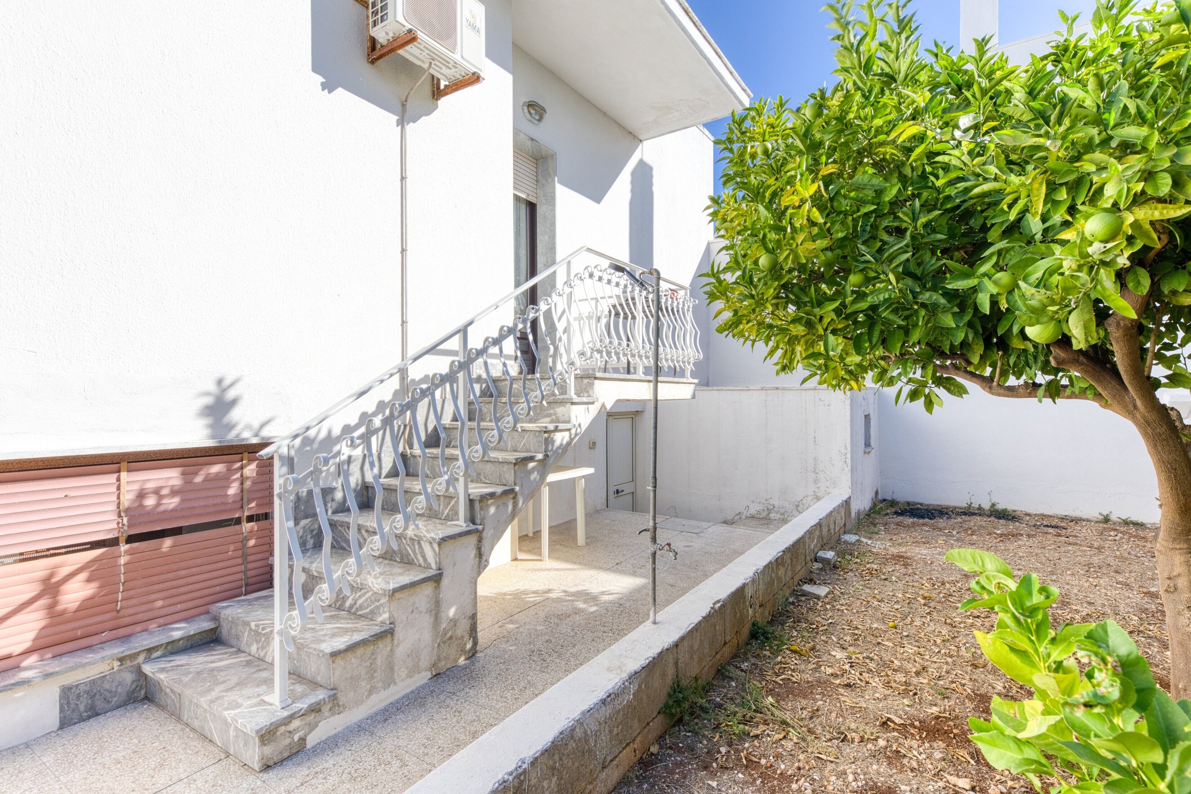 Un edificio blanco con una escalera que lleva a una puerta, un árbol y un pequeño jardín.