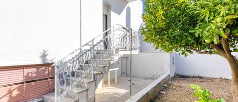 Un edificio blanco con una escalera que lleva a una puerta, un árbol y un pequeño jardín.