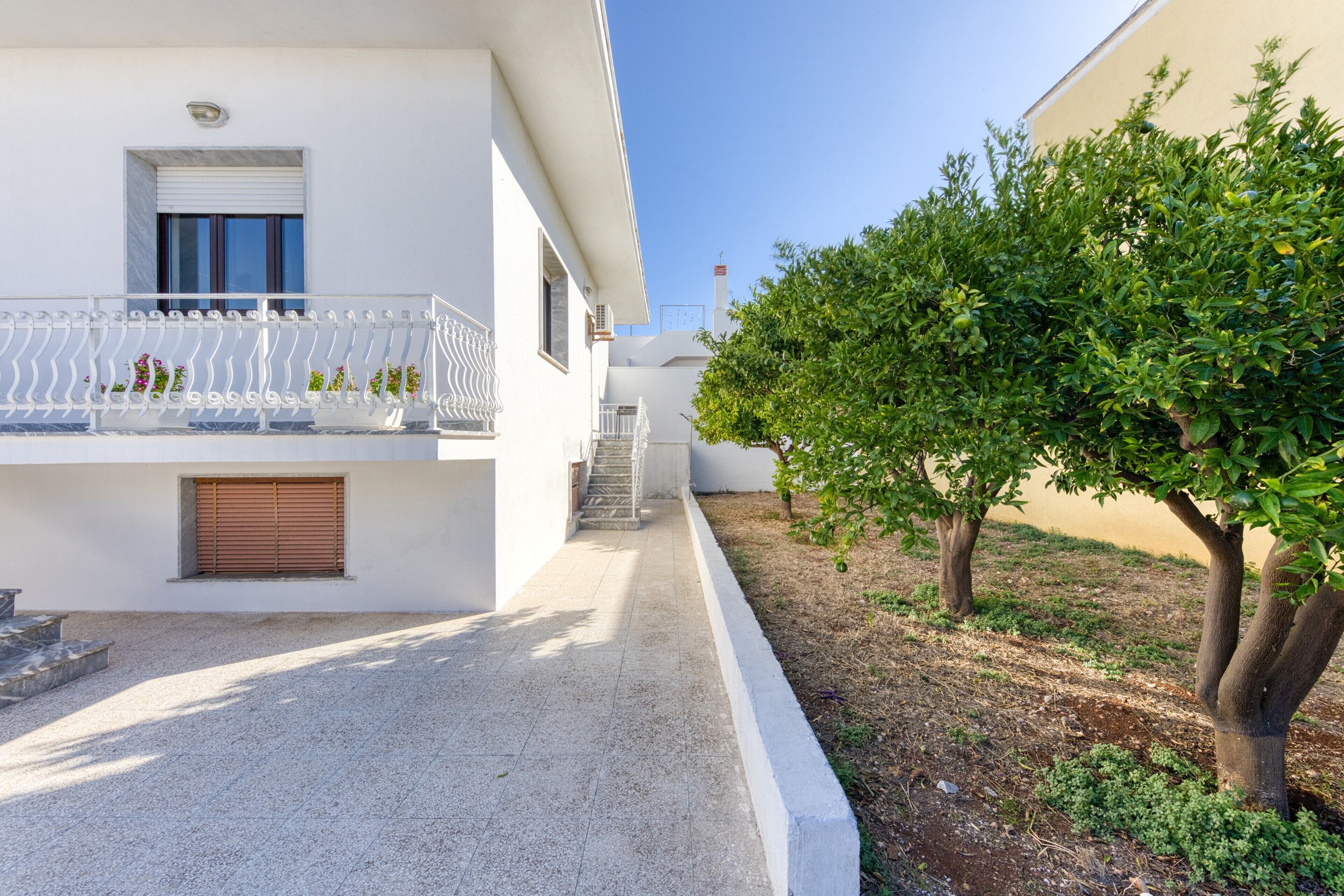 A white building with a balcony, a staircase, and a tree in the foreground.