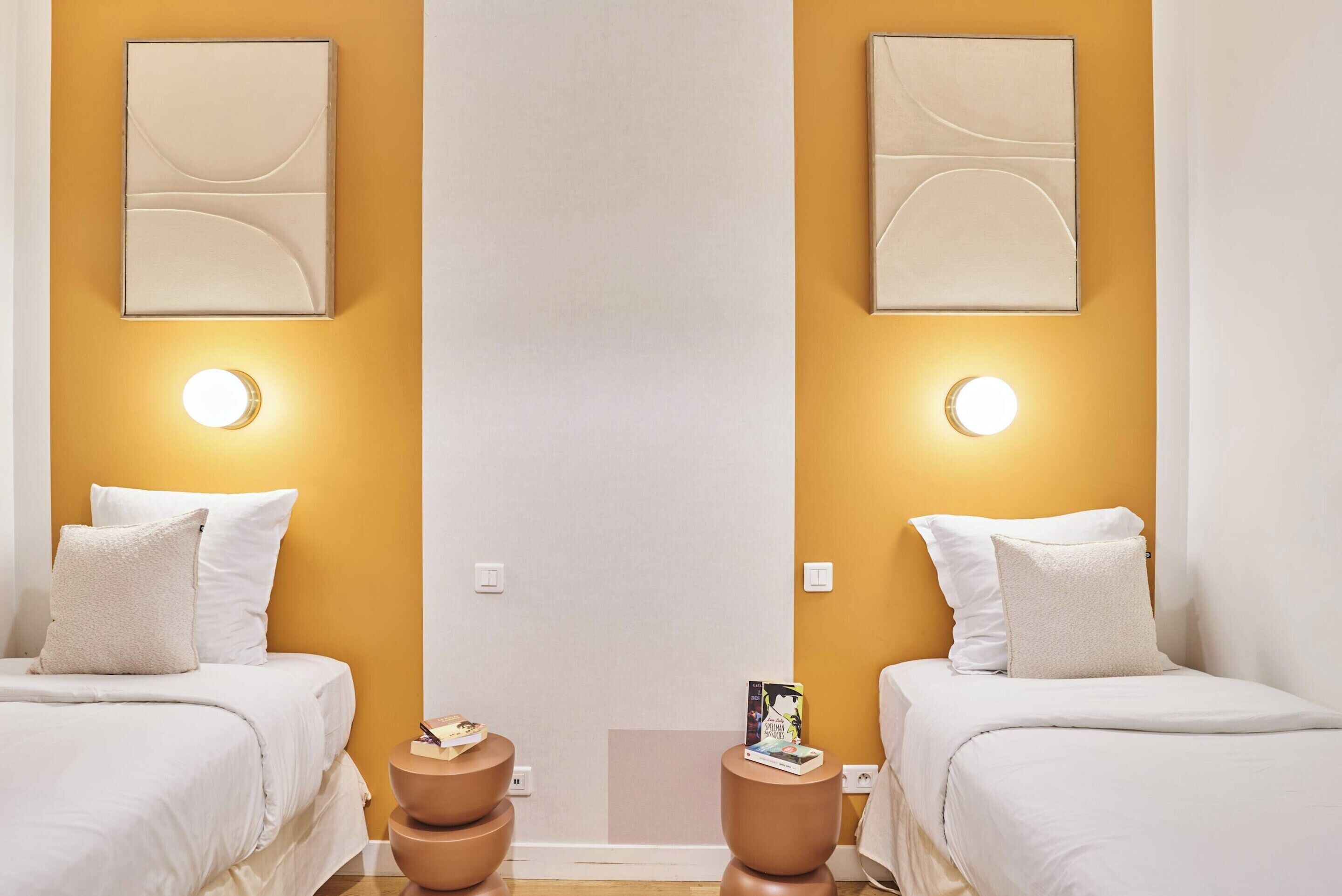 A hotel room with two beds, a small table, and a wall-mounted light fixture.