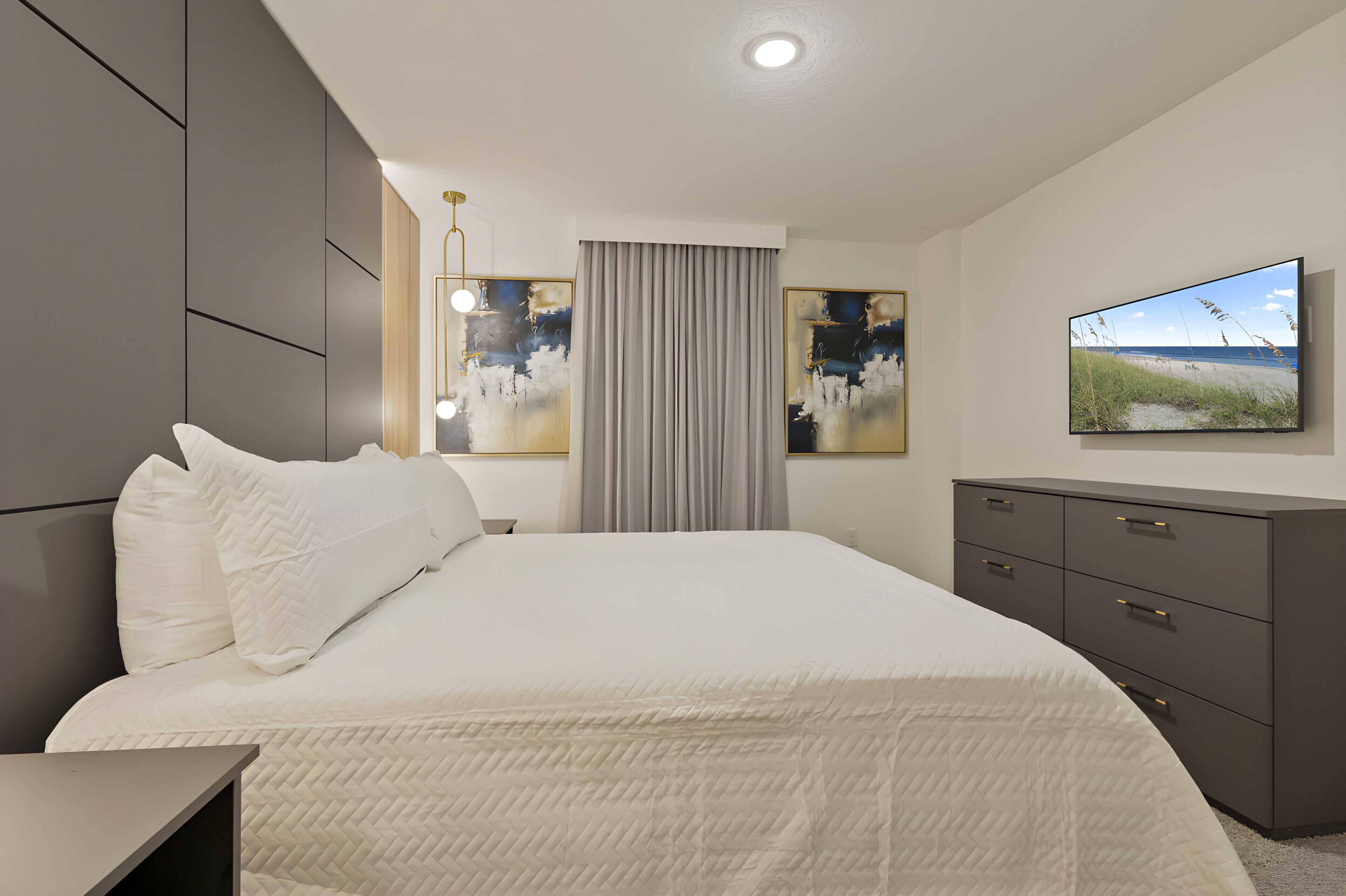 Een moderne slaapkamer met een groot bed, een dressoir en een flatscreen televisie aan de muur.
