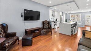 A modern living room with a flat-screen TV, leather sofas, a wooden entertainment unit, and a kitchen in the background. - Renovated 2Level Flat+H St+Laundry (Washington)