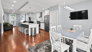 A modern kitchen with a central island, stainless steel appliances, and a dining area with white chairs and a grey table. - Renovated 2Level Flat+H St+Laundry (Washington)